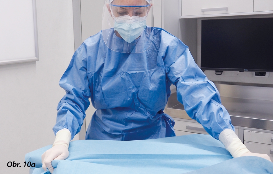 Příprava operačního stolku: Instrumentářka zakrývá operační stolek jednorázovými rouškami přes povrchy, kterých se mohou členové týmu během operace pravděpodobně dotknout.